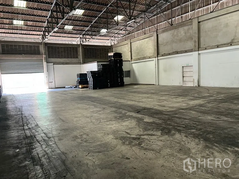 Warehouse for rent in Mueang Samut Prakan, Samut Prakan - Spacious warehouse interior with high steel-truss roof, smooth concrete floor and a large roller shutter entry.