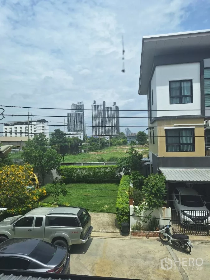 联排别墅 出租在Mueang Samut Prakan, Samut Prakan - 二楼视角：前院草坪与车道，远处可见高层建筑。