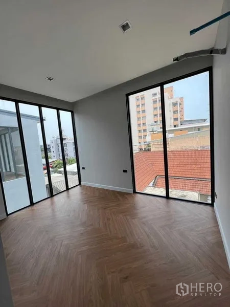 Home Office for sale in Wang Thonglang, Bangkok - Corner bedroom with herringbone wood flooring and full-height windows overlooking the neighborhood.