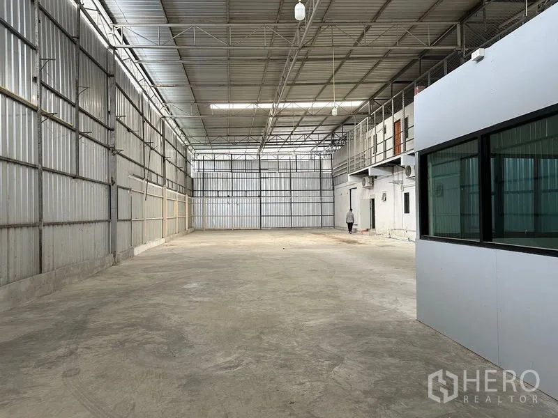 Warehouse for rent in Bang Khun Thian, Bangkok - Open storage bay with mezzanine offices, AC units and bright overhead lighting inside a metal-clad warehouse.
