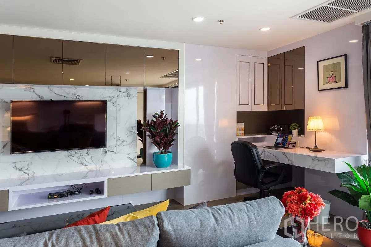 Condominium for rent or sale in Watthana, Bangkok - Home office nook with a marble desk beside the sofa and a built-in TV wall with planters.