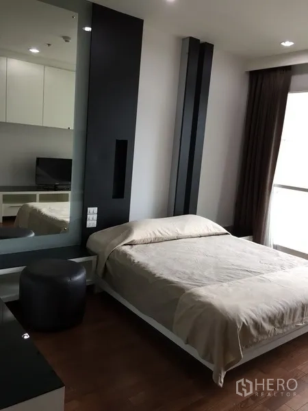 Condominium for rent in Pathum Wan, Bangkok - Minimal bedroom with wood flooring, large mirror panel, dark curtains and a platform bed.