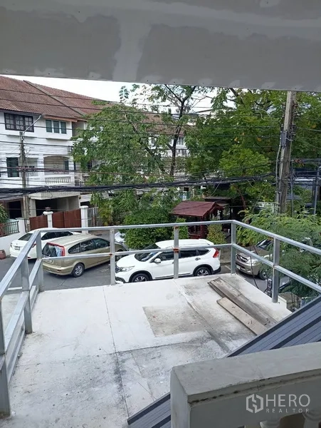 联排别墅 出租或出售在Wang Thonglang, Bangkok - 从楼上阳台俯瞰安静的住宅街道，绿树与停放车辆一览无余。