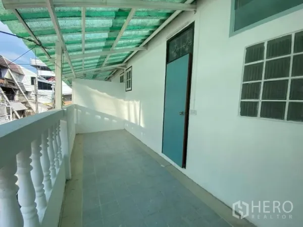 ทาวน์เฮาส์ ให้เช่าในWatthana, Bangkok - ระเบียงยาวมีหลังคาใยเขียว ราวระเบียงสีขาว และประตูเข้าด้านข้าง.