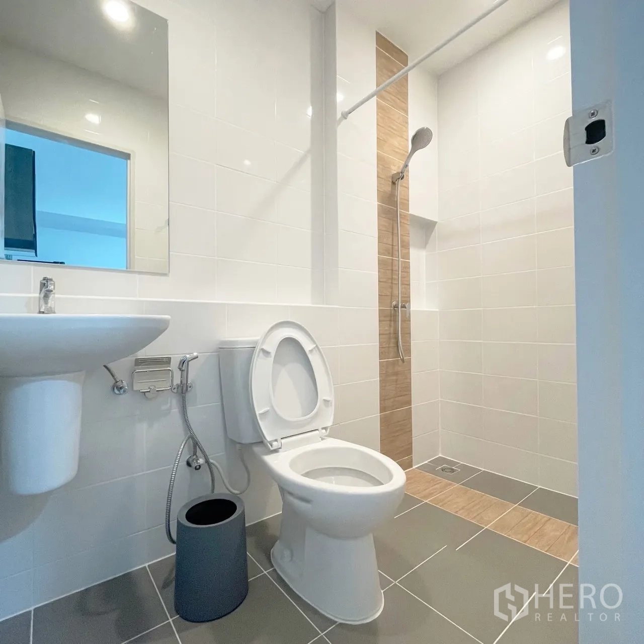 Townhouse for rent in Bang Phli, Samut Prakan - Bright bathroom with pedestal sink, toilet, handheld bidet, and a walk-in shower with beige accent tiles.