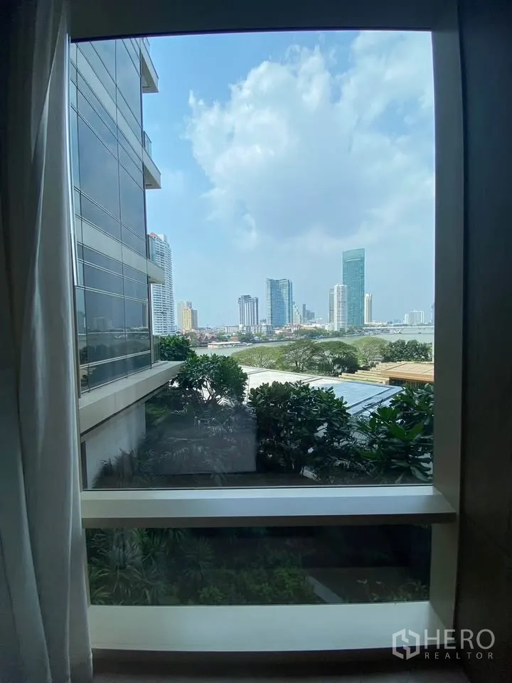 Condominium for rent in Sathon, Bangkok - City skyline and river view framed by a large window with greenery below.