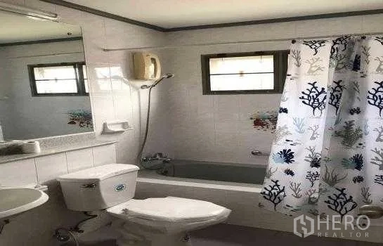 Detached House for rent in Khlong Sam Wa, Bangkok - White tiled bathroom featuring a bathtub, shower curtain, vanity mirror and water heater.