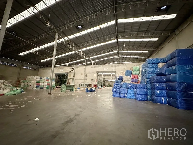 工厂 出租在Bang Bua Thong, Nonthaburi - 生产与仓储区域，钢桁架屋顶，成堆打包物料整齐摆放。