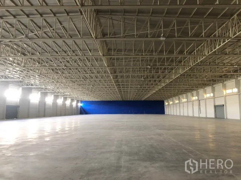 Warehouse for rent in Bang Sao Thong, Samut Prakan - Long clear warehouse hall with bright side windows and a blue partition at the end.