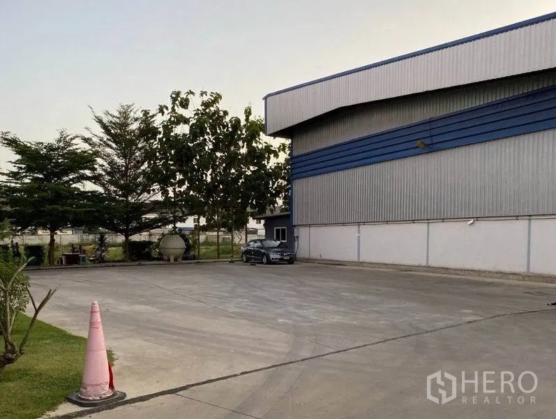 Warehouse for rent in Lat Krabang, Bangkok - Wide concrete yard beside a metal-clad warehouse with parking area and trees.