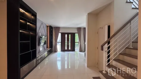 บ้าน ให้เช่าหรือขายในSaphan Sung, Bangkok - พื้นที่นั่งเล่นแบบโอเพ่นสเปซ ปูพื้นกระเบื้องเงา ตู้ทีวียาว และบันไดราวสีขาวขึ้นสู่ชั้นบน.