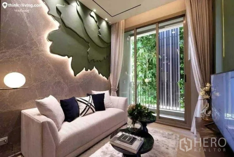 Condominium for sale in Bang Kho Laem, Bangkok - Stylish living room with feature wall art, light sofa, sliding glass doors to a balcony and green wall.