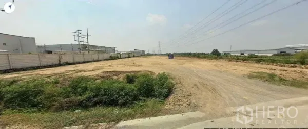 Land for sale in Sai Noi, Nonthaburi - Wide cleared earth plot with grass verge and a high-voltage transmission tower on the horizon.