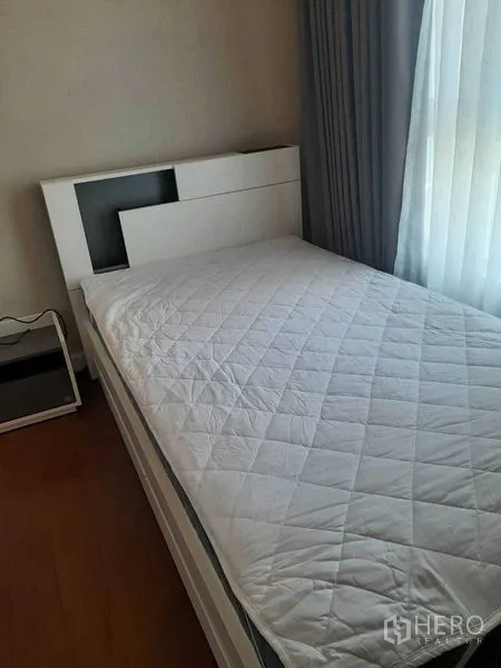 Condominium for rent or sale in Huai Khwang, Bangkok - Single bedroom with quilted bedding beside sheer curtains and wood flooring