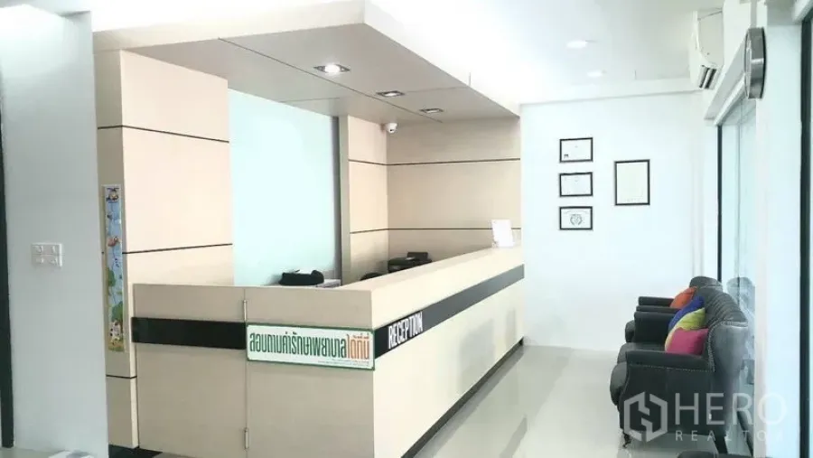 Shophouse for rent in Khan Na Yao, Bangkok - Reception area with long built-in counter, certificate frames on the wall and seating by the glass facade.