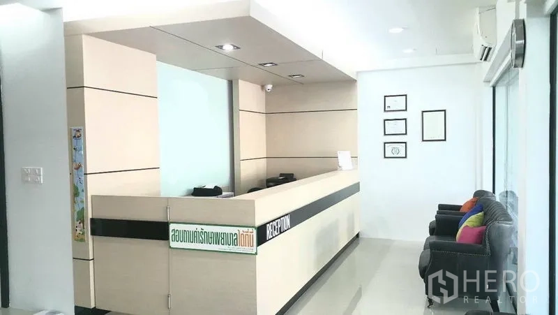 Shophouse for rent in Khan Na Yao, Bangkok - Reception area with long built-in counter, certificate frames on the wall and seating by the glass facade.