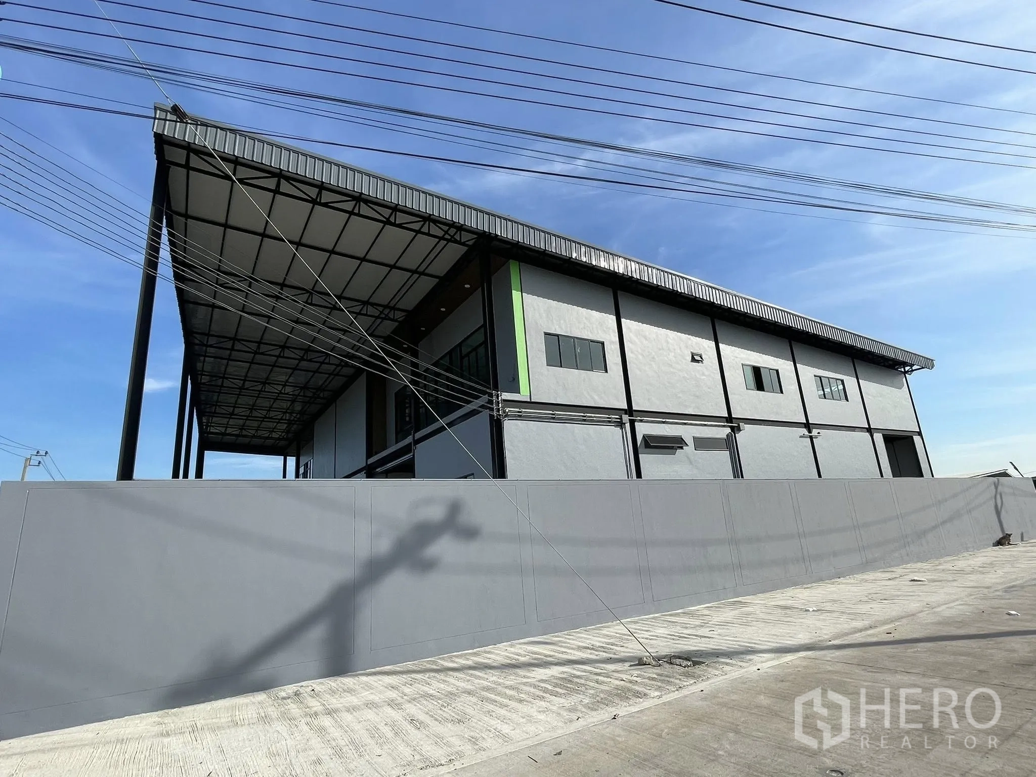 Warehouse for rent in Phra Samut Chedi, Samut Prakan - Side elevation of the warehouse behind a high boundary wall and power lines.