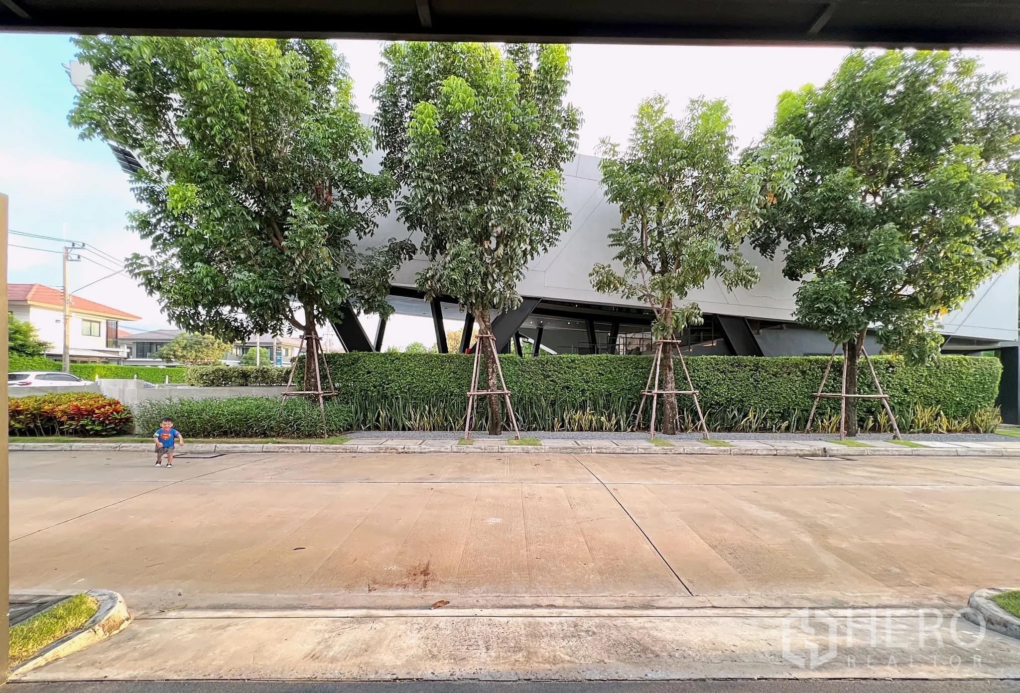 บ้าน ให้เช่าหรือขายในLam Luk Ka, Pathum Thani - มุมมองจากโรงจอดรถสู่คลับเฮาส์ภูมิทัศน์ฝั่งตรงข้ามถนนร่มรื่น