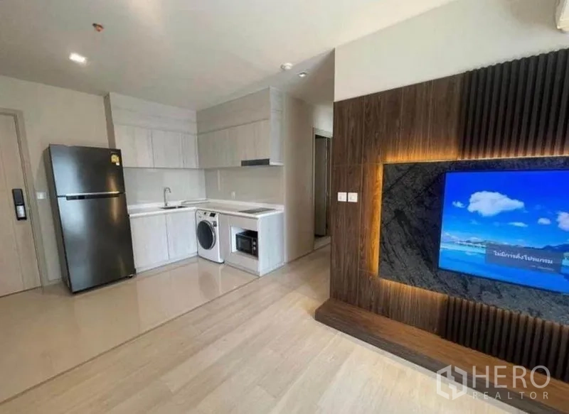 Condominium for rent or sale - Open-plan kitchen and living room with TV feature wall and light wood floors.
