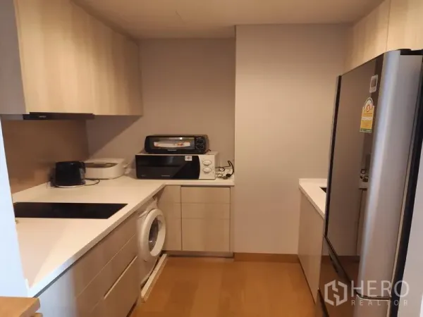 Condominium for rent in Khlong Toei, Bangkok - Modern galley kitchen with built-in cabinets, induction hob, washer and large stainless fridge.