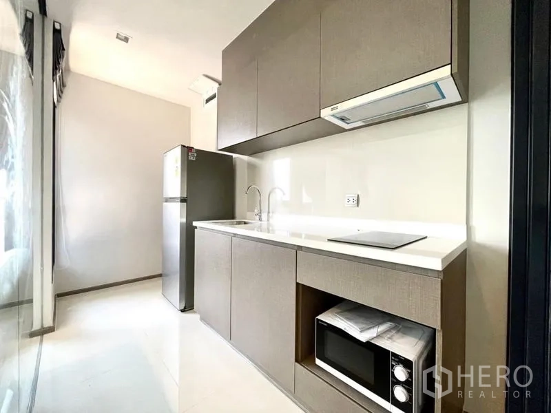Condominium for rent in Chatuchak, Bangkok - Sleek closed kitchen with cabinets, sink, cooktop, hood, microwave and refrigerator.