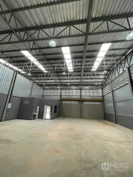 Warehouse for rent in Phra Samut Chedi, Samut Prakan - Deep interior view toward rear roller shutters, skylights, and a wide clear‑span floor area.