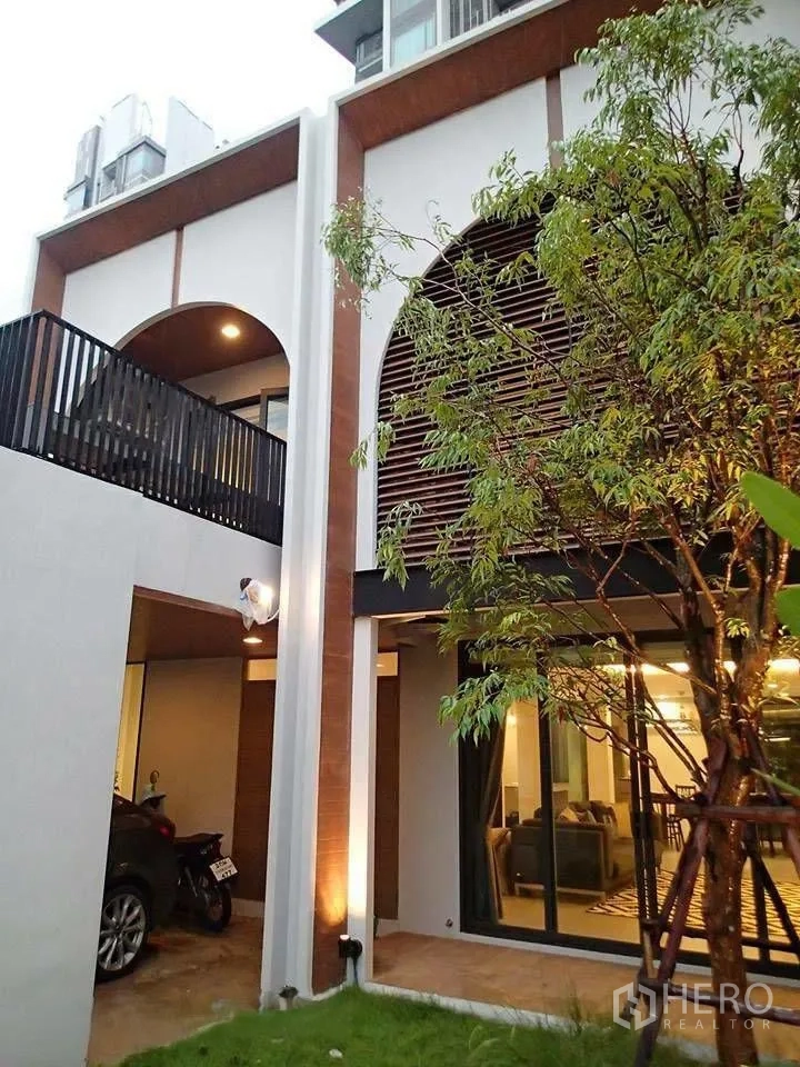 Townhouse for rent in Watthana, Bangkok - Contemporary townhouse facade with arched balcony, wood slats, carport, and garden.