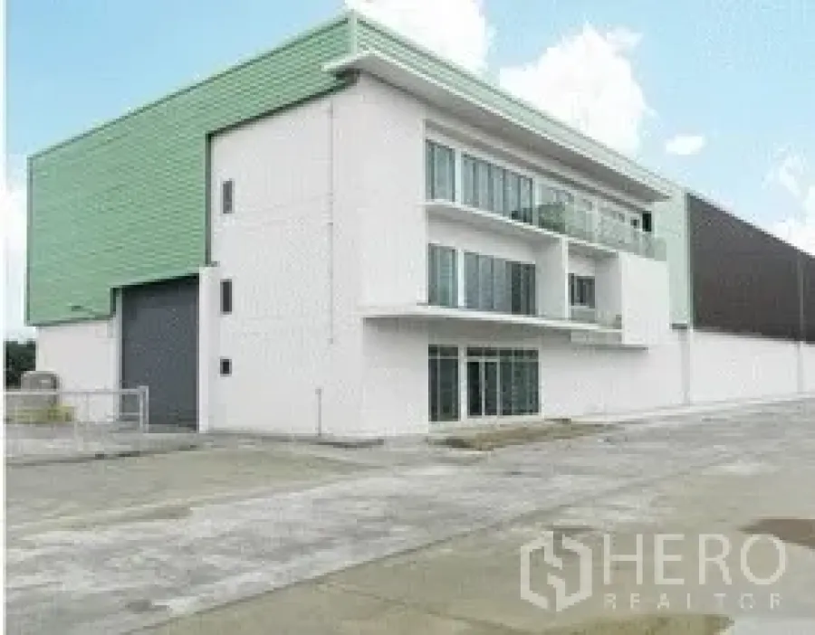 Warehouse for rent in Nonthaburi - Modern warehouse with three-storey office block, green metal cladding, large roller shutter, and wide concrete loading yard in Nonthaburi.