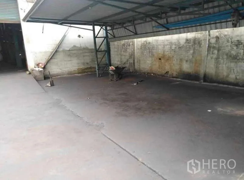 Warehouse for rent in Prawet, Bangkok - Covered loading bay with metal canopy and spacious concrete yard for trucks.