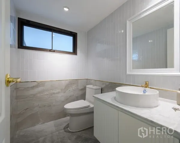Condominium for sale in Watthana, Bangkok - Modern bathroom with marble tiles, a window, round basin and gold fixtures.