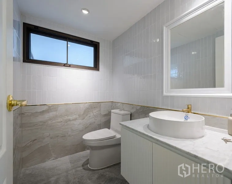 Condominium for sale in Watthana, Bangkok - Modern bathroom with marble tiles, a window, round basin and gold fixtures.