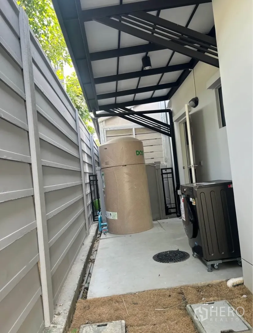 บ้านแฝด for rent in Bang Phli, Samut Prakan - พื้นที่ซักล้างด้านข้างมีหลังคา แทงก์น้ำ และเครื่องซักผ้าข้างรั้วสูงเพื่อความเป็นส่วนตัว