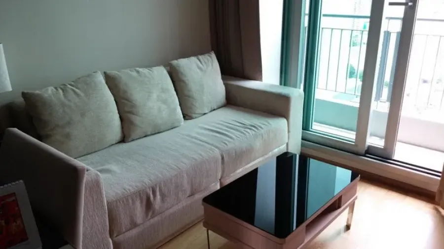 Condominium for rent in Ratchathewi, Bangkok - Bright living room with beige sofa, sleek black glass coffee table, and sliding doors to the balcony.