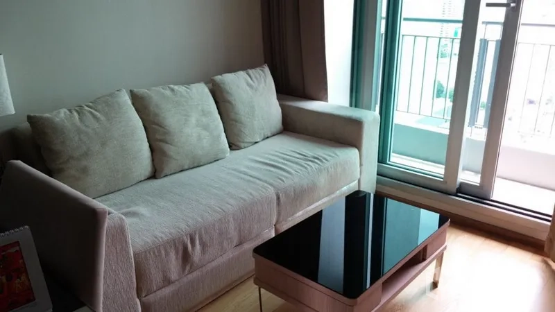 Condominium for rent in Ratchathewi, Bangkok - Bright living room with beige sofa, sleek black glass coffee table, and sliding doors to the balcony.