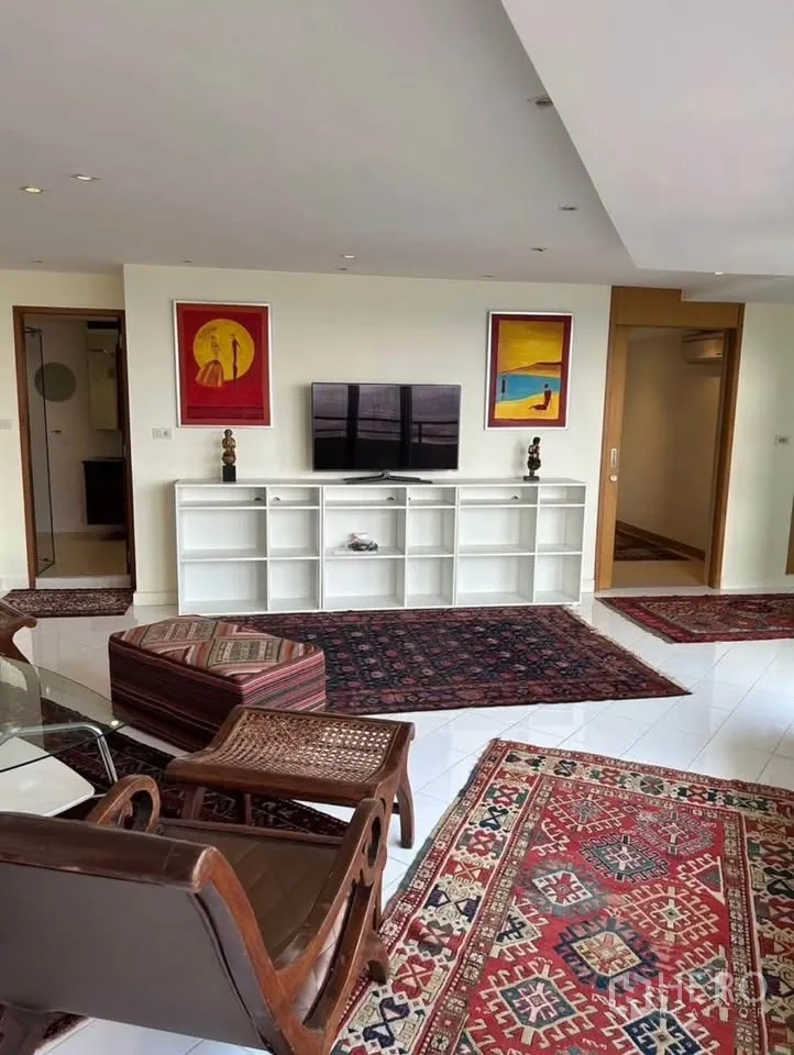 Condominium for rent or sale in Yan Nawa, Bangkok - Living room with white shelving wall, TV and multiple Persian-style rugs.