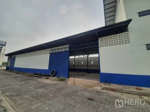 工厂 出租在Bang Bua Thong, Nonthaburi - 蓝白配色仓库侧立面，设有有顶装卸位与卷门。