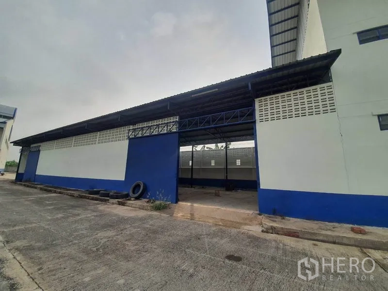工厂 出租在Bang Bua Thong, Nonthaburi - 蓝白配色仓库侧立面，设有有顶装卸位与卷门。