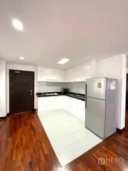 คอนโด ให้เช่าในWatthana, Bangkok - ครัวสีขาวกะทัดรัด เคาน์เตอร์หินสีดำ ตู้เก็บของ เตา และตู้เย็นขนาดใหญ่ใกล้ประตู