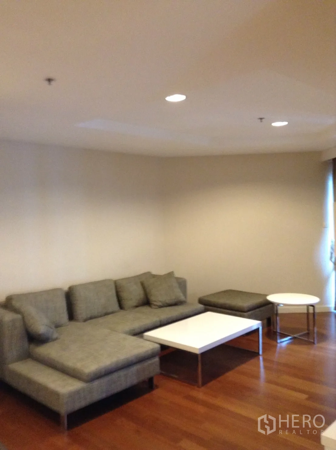 Condominium for rent in Huai Khwang, Bangkok - Spacious lounge with an L-shaped fabric sofa and nesting coffee tables on timber floors.