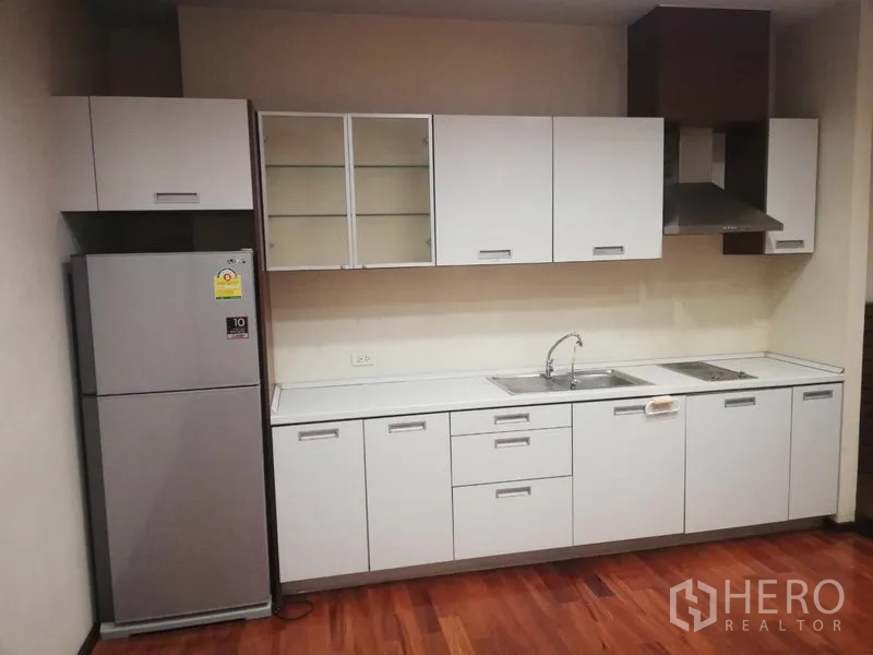 Condominium for rent in Watthana, Bangkok - Linear kitchen with white cabinetry, double sink, range hood and stainless refrigerator.