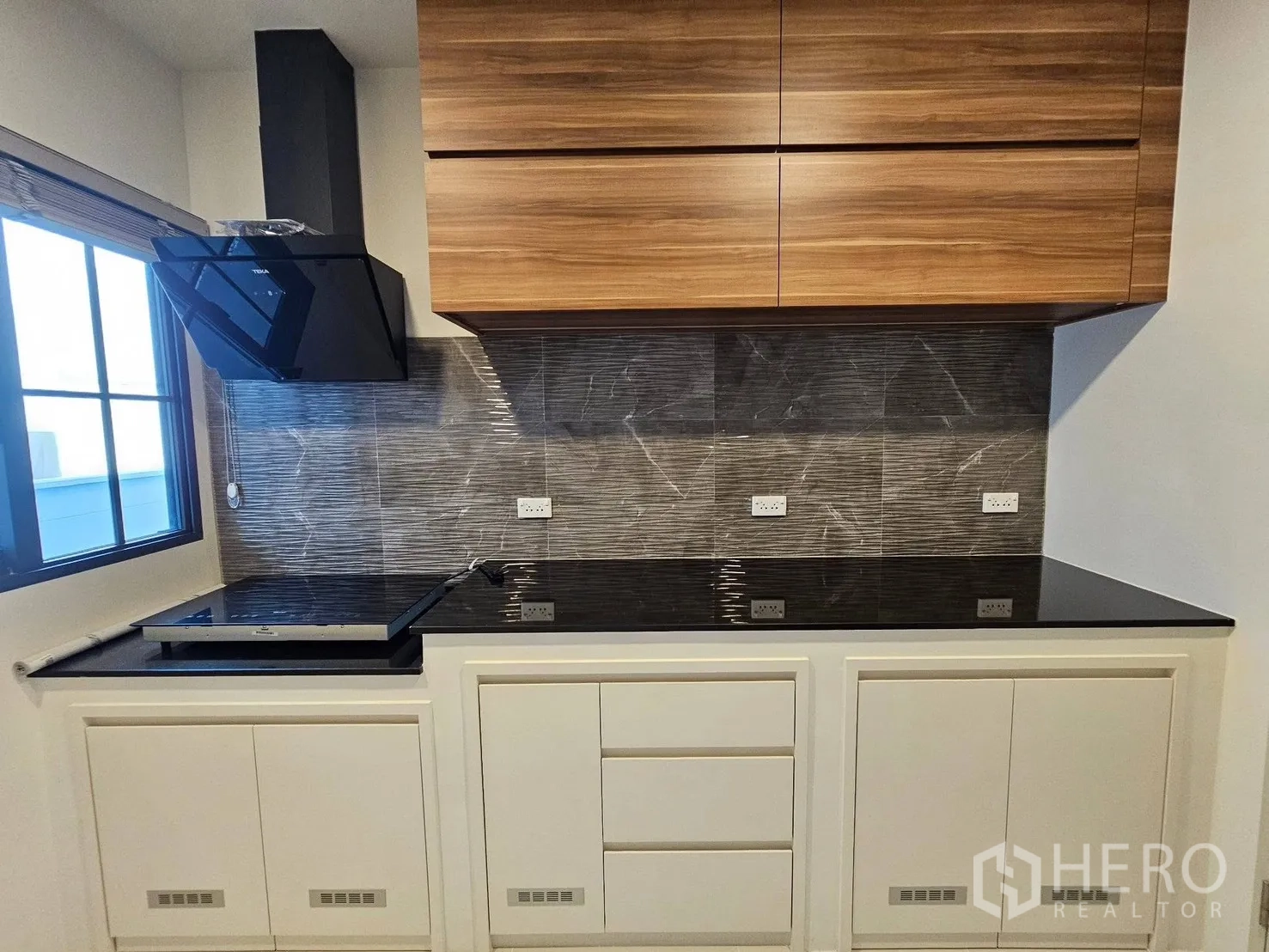 Detached House for rent or sale in Bang Phli, Samut Prakan - Modern kitchen with black granite countertops, wood cabinets, tiled backsplash, stove and hood beside a window.