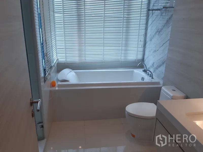 คอนโด ให้เช่าหรือขายในKhlong Toei, Bangkok - ห้องน้ำพร้อมอ่างอาบน้ำ โถสุขภัณฑ์ และอ่างล้างหน้า ข้างหน้าต่างบานมู่ลี่และผนังหินอ่อน