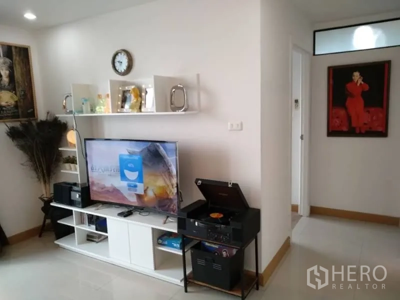 Condominium for rent in Watthana, Bangkok - Bright living room with TV console, wall shelves and a hallway leading to bedrooms.