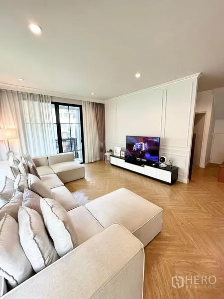 Detached House for sale in Prawet, Bangkok - Bright living room with large sectional sofa, TV wall and herringbone wood flooring.