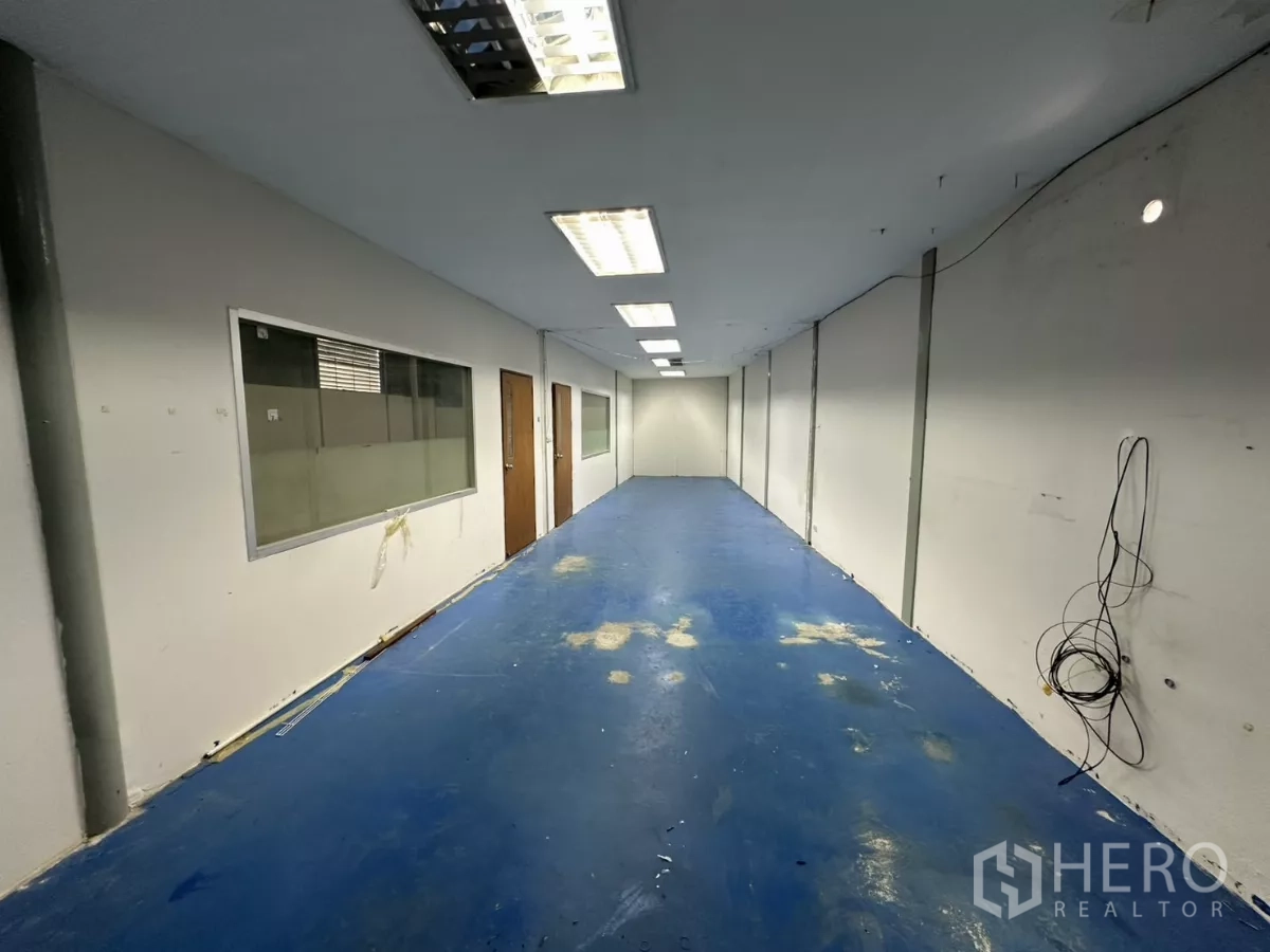 Warehouse for rent in Suan Luang, Bangkok - Office corridor perspective with blue flooring, timber doors, and visible wall cabling.