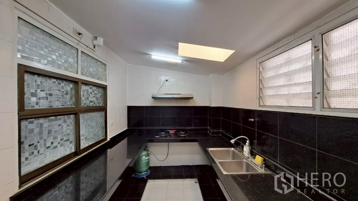 Townhouse for rent in Watthana, Bangkok - U-shaped Thai kitchen with gas hob, black wall tiles and skylight.