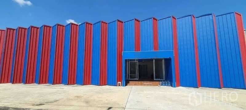 工厂 出租或出售在Lat Krabang, Bangkok - 红蓝金属外立面的工厂，前方为宽阔混凝土场地与晴朗天空。