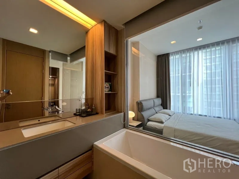 Condominium for rent in Watthana, Bangkok - Contemporary bathroom featuring a vanity with storage and a bathtub beside a window to the bedroom.