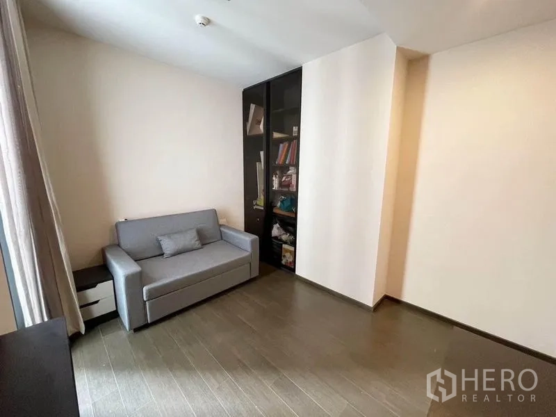 Condominium for rent in Pathum Wan, Bangkok - Versatile second bedroom with gray sofa bed, built-in shelving, and natural light.