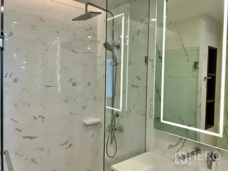 Condominium for rent in Khlong Toei, Bangkok - Bathroom with glass shower enclosure, rain shower head and backlit mirror over vanity.